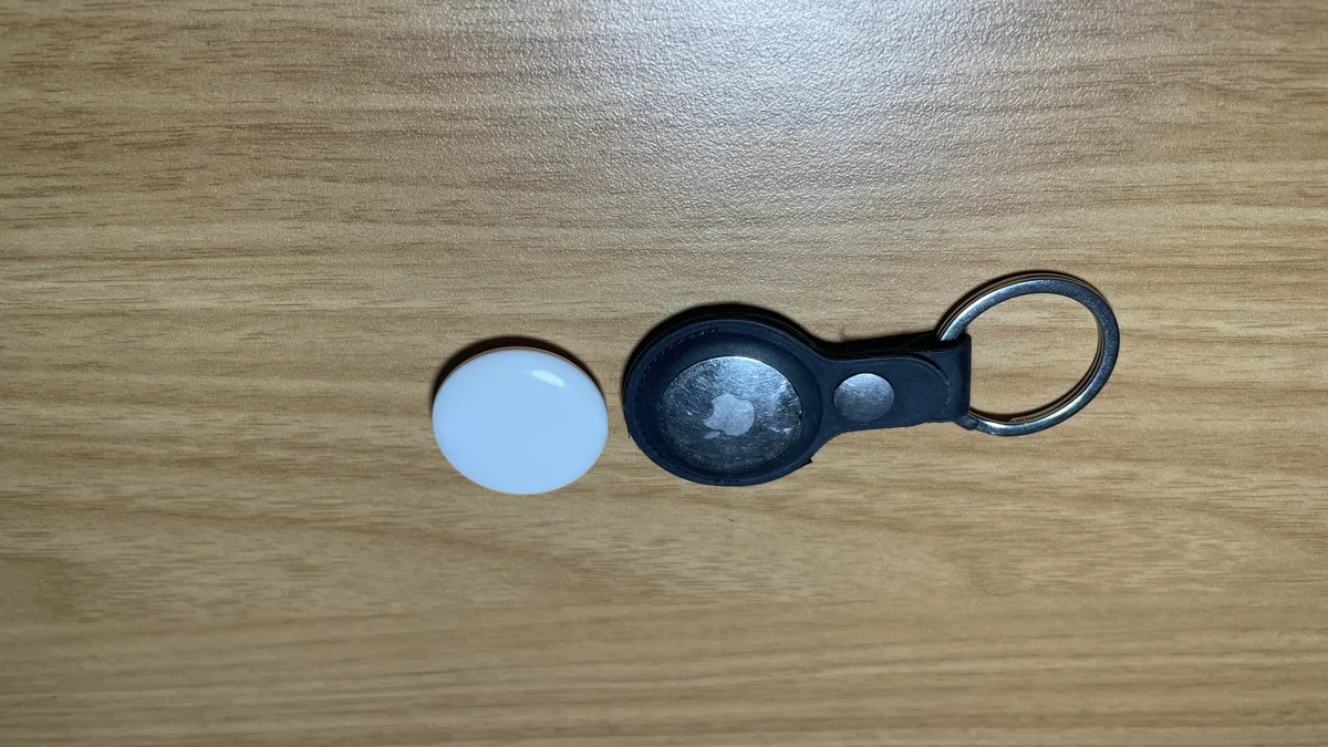 Two Apple AirTags on a wooden desk, including one fitted inside a black key-ring holder