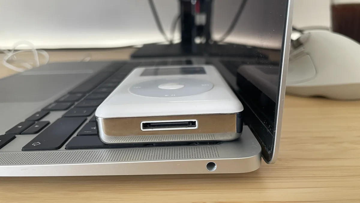 Close-up of an M1 MacBook Air headphone jack beside a classic iPod on a desk